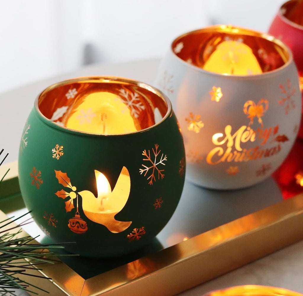 Green and white frosted glass tealight holders with gold dove and Merry Christmas designs glowing warmly.