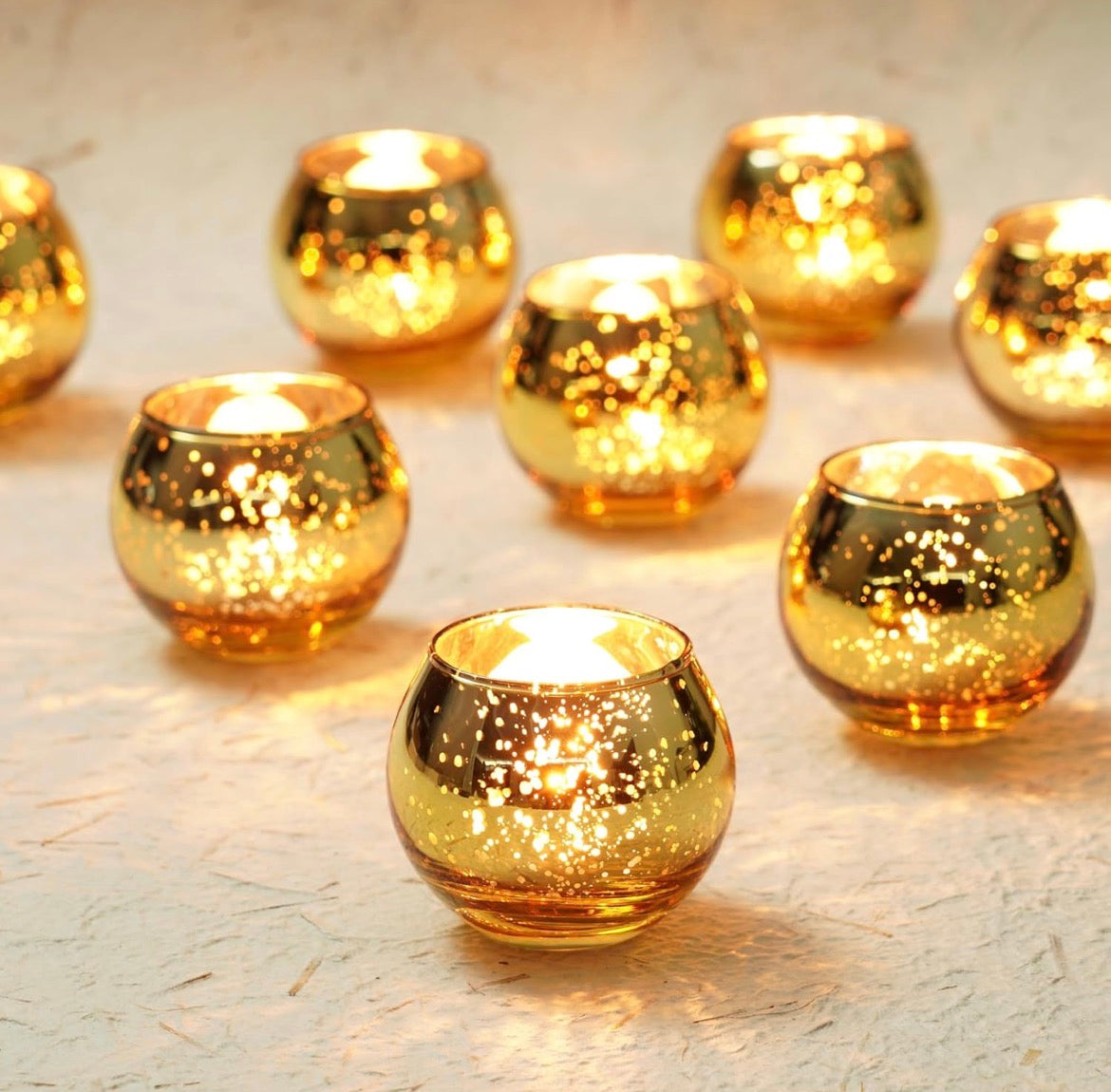 Set of 12 gold mercury glass candle holders arranged together with glowing coconut-wax tea lights.