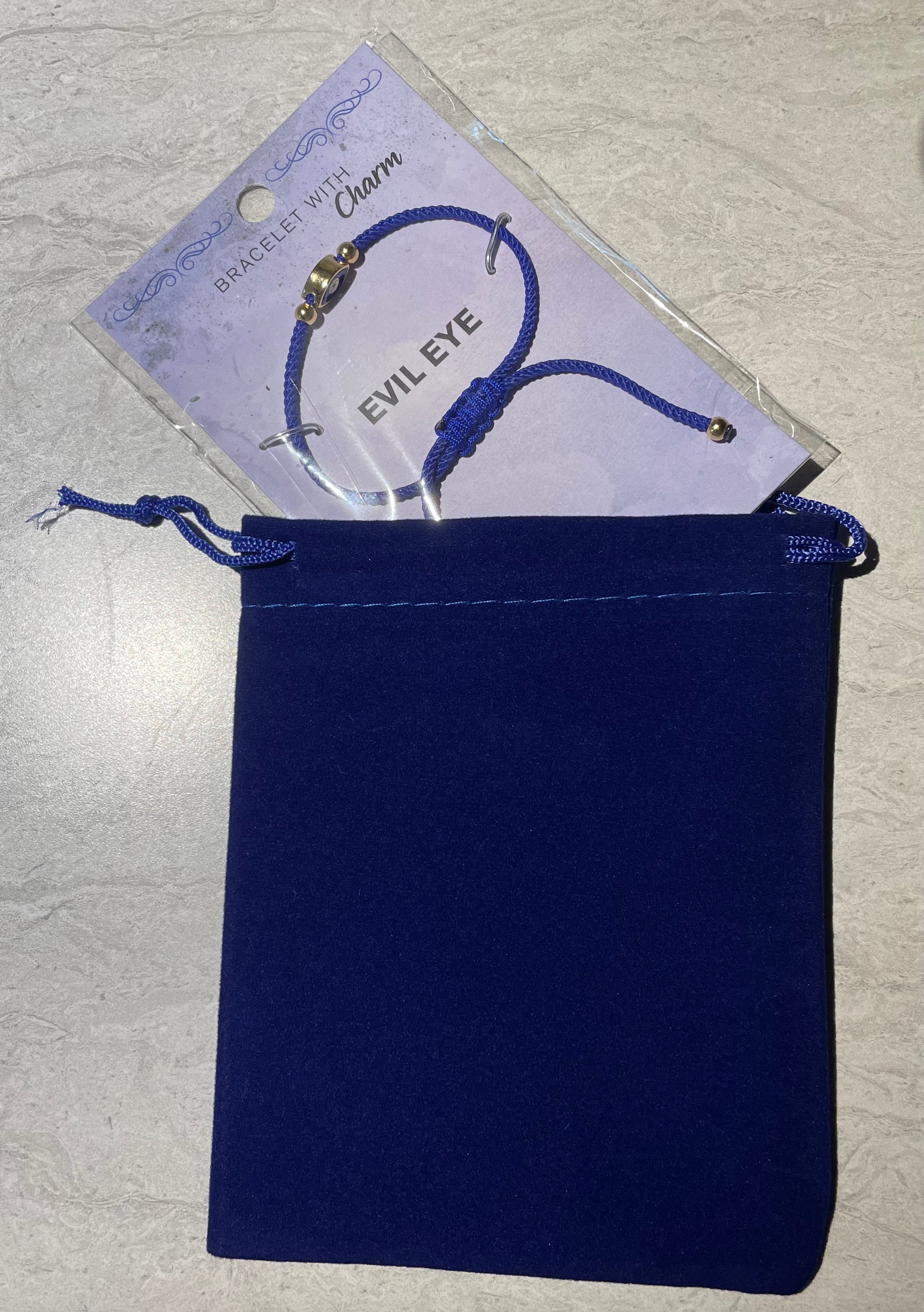 Blue bracelet with 'Evil Eye' charm on a blue drawstring pouch against a gray background